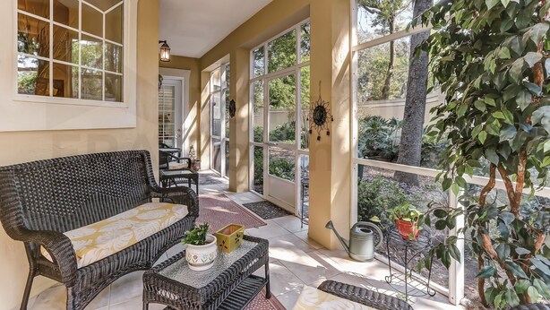 A sunlit covered patio with wicker furniture, large windows, and potted plants. - Exclusive Gated Villas at Summer Beach, Short Walk to the Beach by RedAwning (Fernandina Beach)