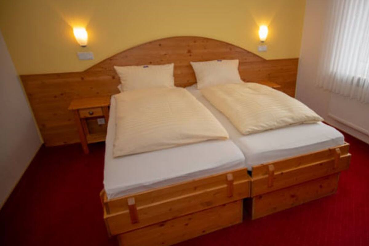 Uma cama de casal com cabeceira e peseira de madeira, duas mesas de cabeceira e luminárias fixadas na parede.