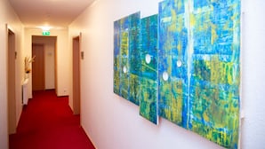 Een gang met een rood tapijt en drie abstracte schilderijen aan de muur.