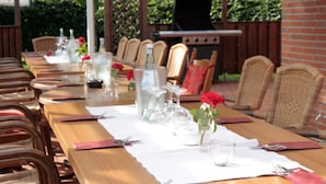 Een lange eettafel met stoelen, een barbecue en een rozenstuk als decoratie.