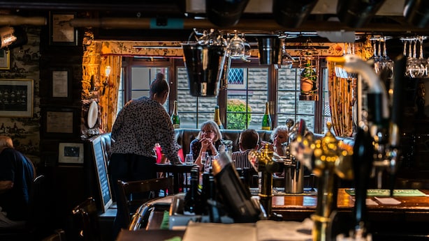 Un bar con un cantinero sirviendo bebidas, paredes de madera y un ambiente acogedor.