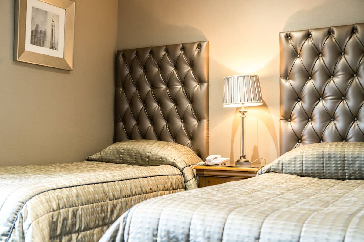 A hotel room with two beds, each with a tufted headboard, a bedside lamp, and a framed picture on the wall.