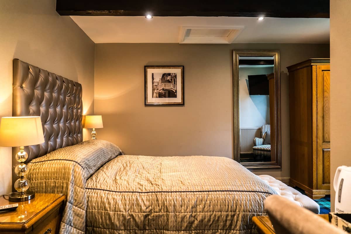 A hotel room with a large bed, two bedside lamps, a framed picture on the wall, a mirror, and a wooden wardrobe.