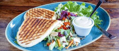 A plate with grilled flatbread, a salad, and a small bowl of sauce on a blue ceramic plate.