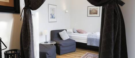 A small, cozy room with a bed, a chair, a small table, and a rug.