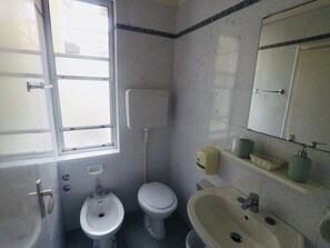 A small, basic bathroom with a toilet, bidet, sink, and a window. - Alevon (Rimini)