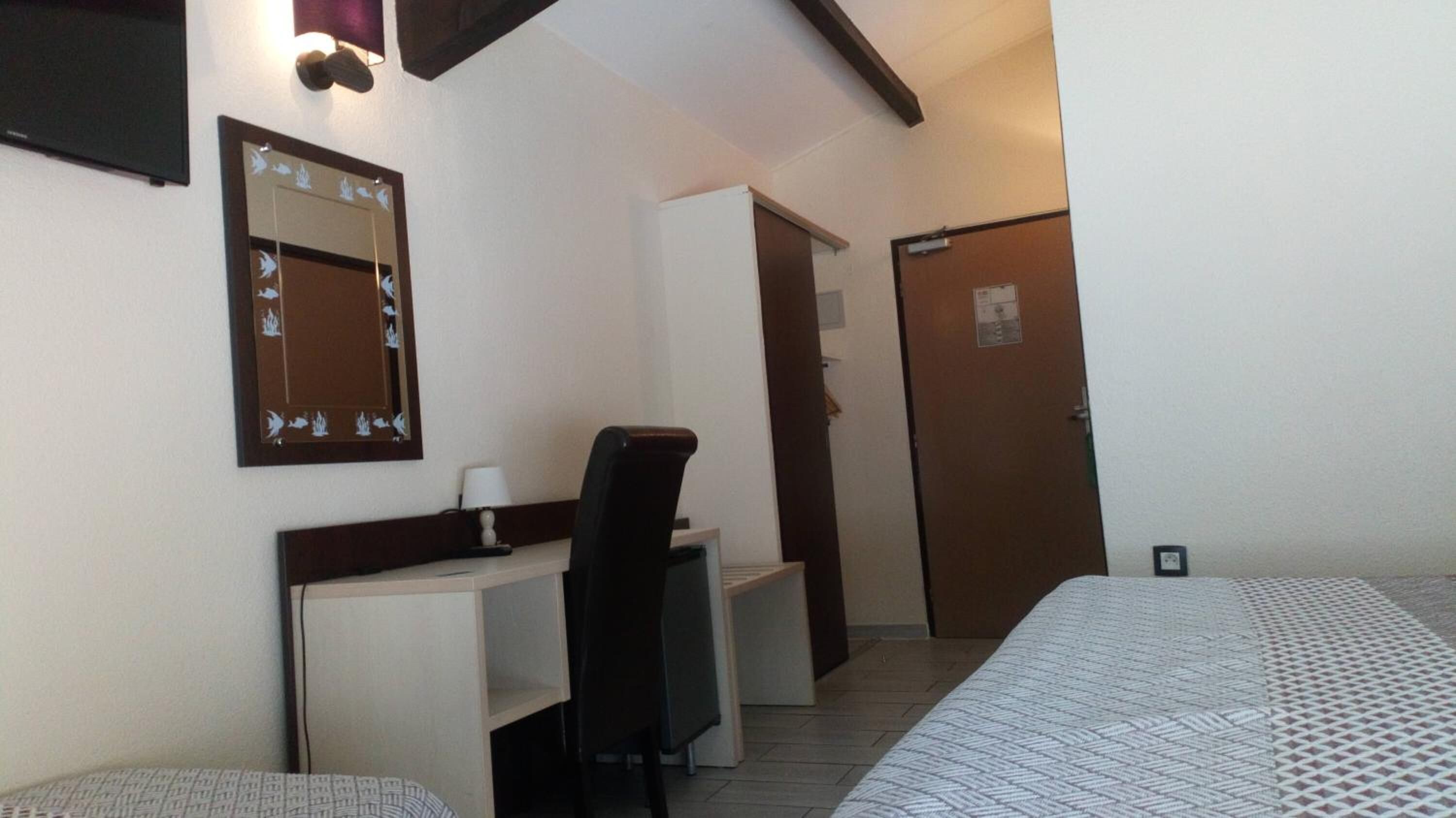 Une chambre d’hôtel avec un lit, un bureau et une chaise, un miroir et une porte.