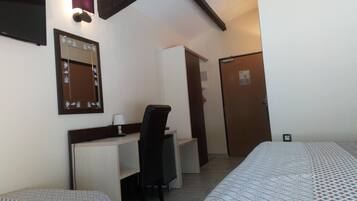 Une chambre d’hôtel avec un lit, un bureau et une chaise, un miroir et une porte.