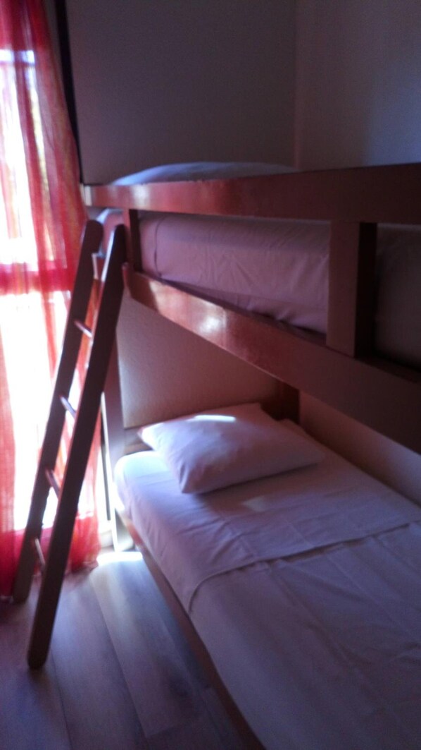 Una cama litera con escalera, ropa de cama blanca y una ventana con cortinas rojas.