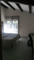 Un dormitorio con cama, ventana con cortinas y vista a la vegetación exterior.