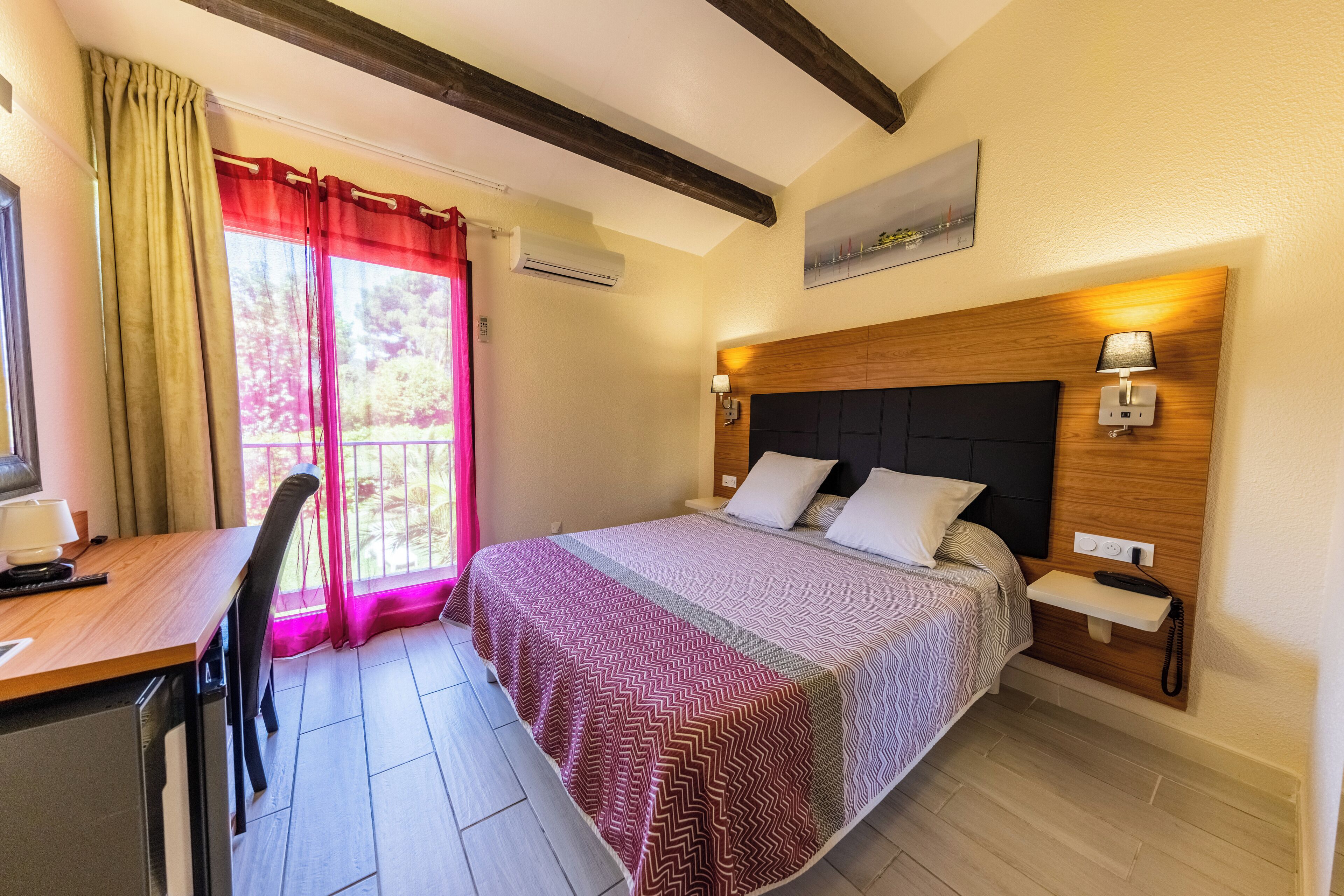 A hotel room with a bed, bedside table, lamp, and a desk with a chair.