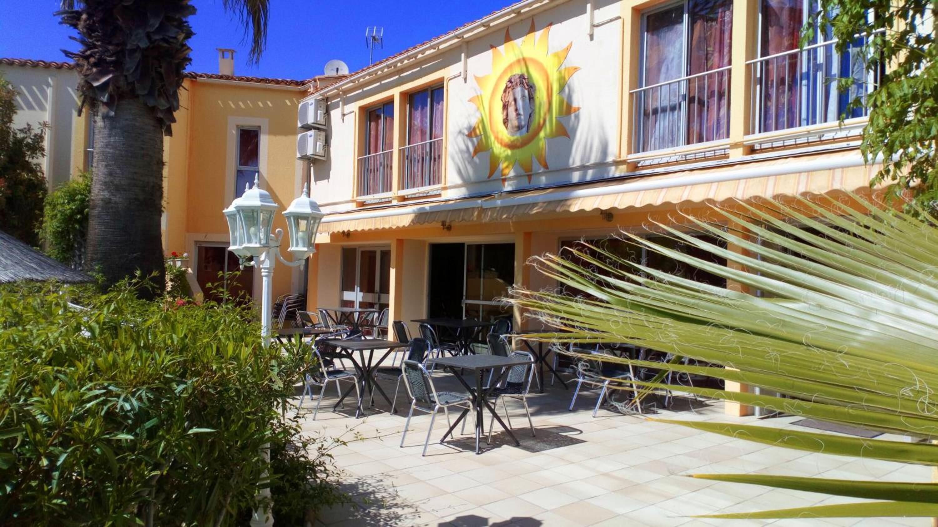 An outdoor café with tables and chairs, a palm tree, and a building with a sun mural.