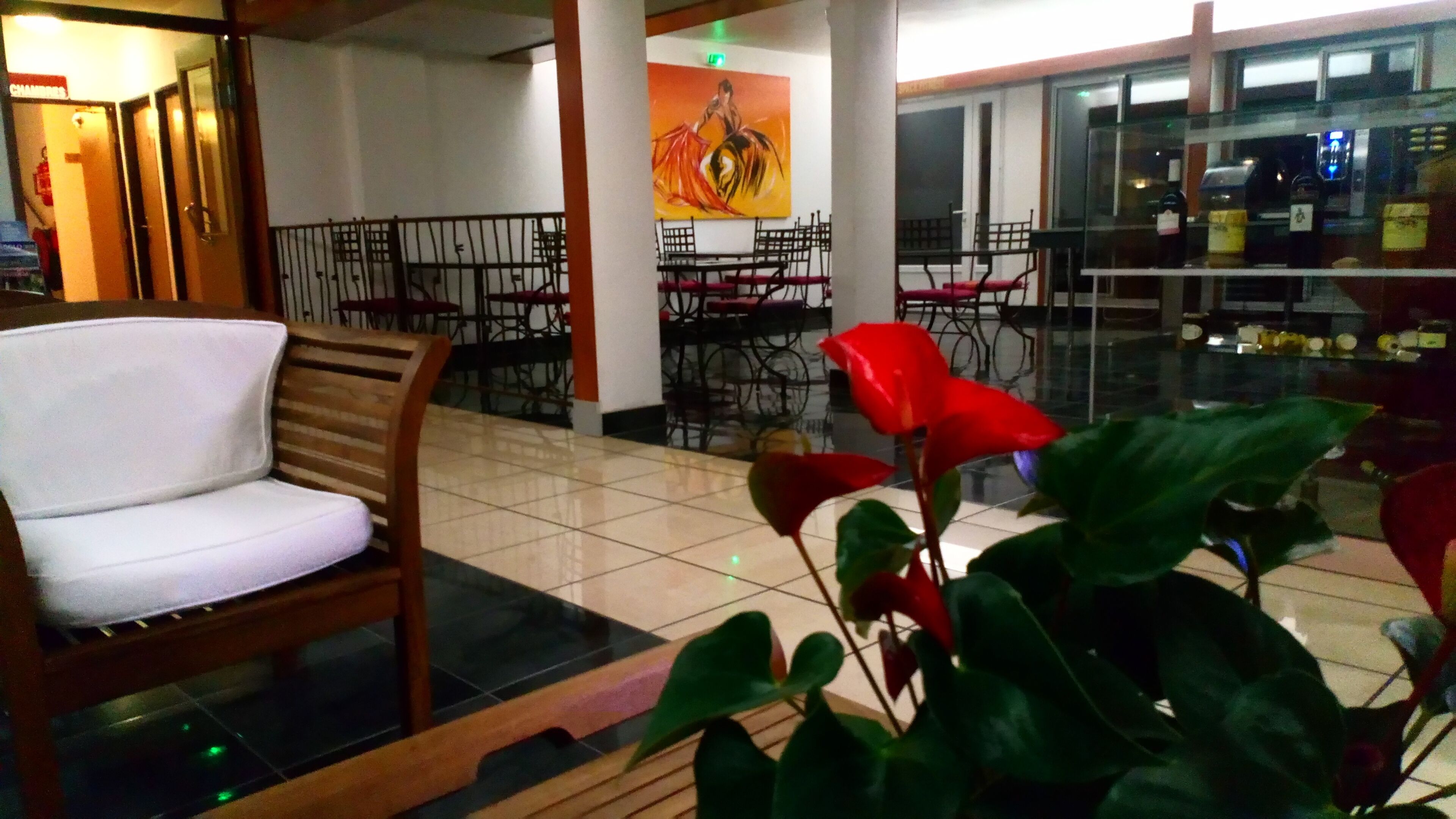 A hotel lobby with a wooden chair, a red flower, and a painting on the wall.