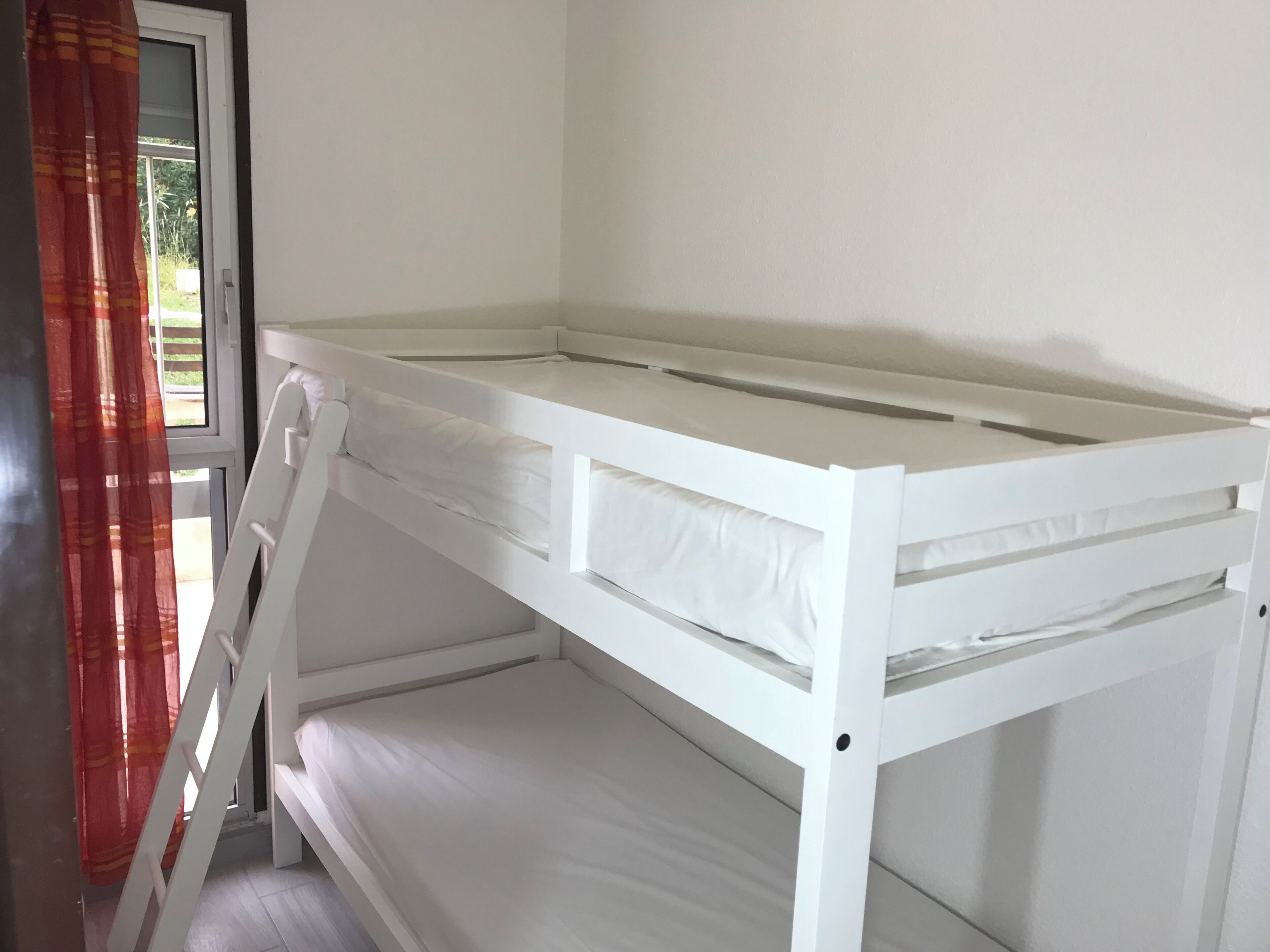 Un lit superposé avec une échelle, des murs blancs et une fenêtre avec des rideaux.