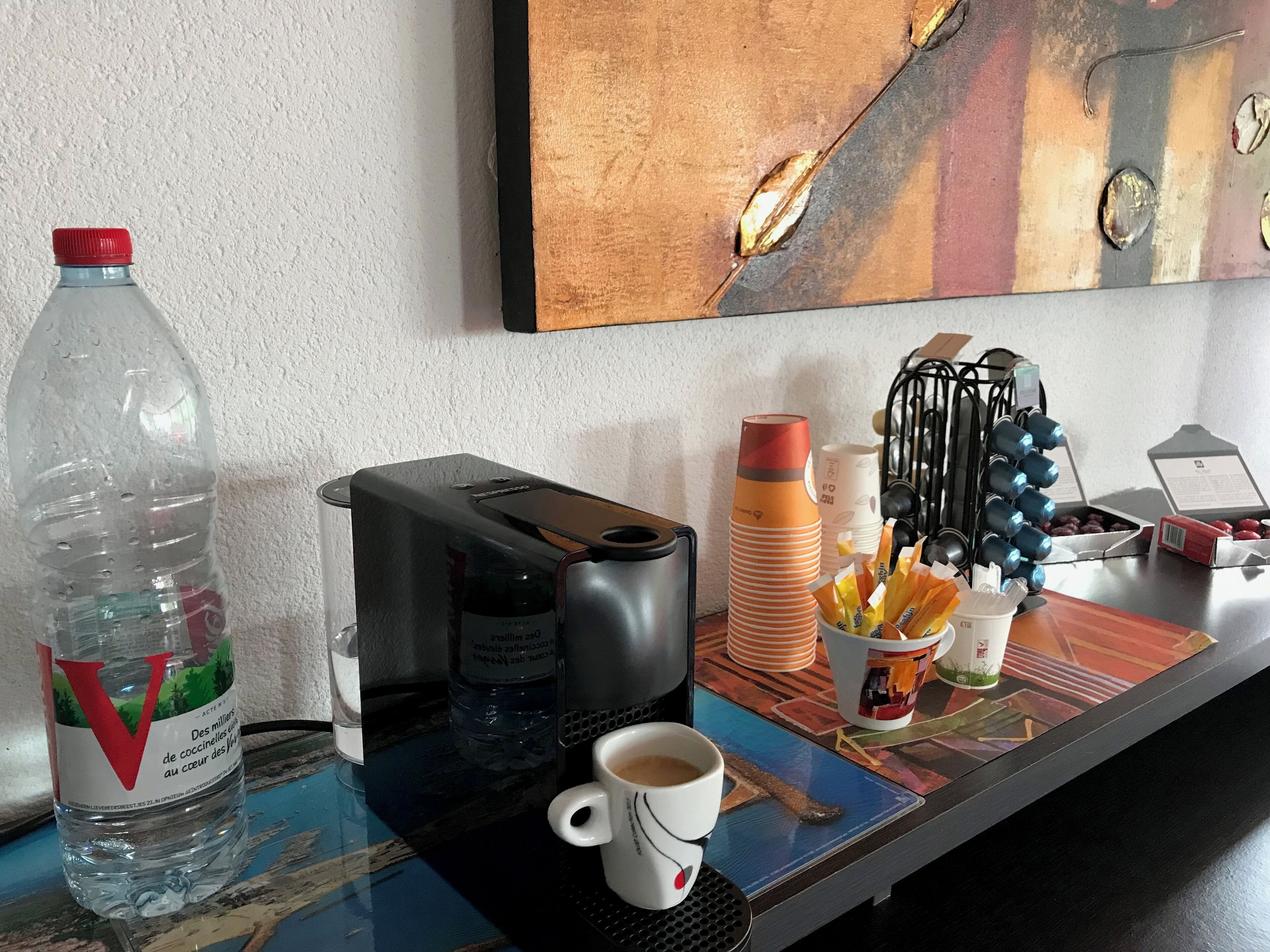 A hotel room with a coffee maker, a cup of coffee, a bottle of water, and a coffee machine on the counter.