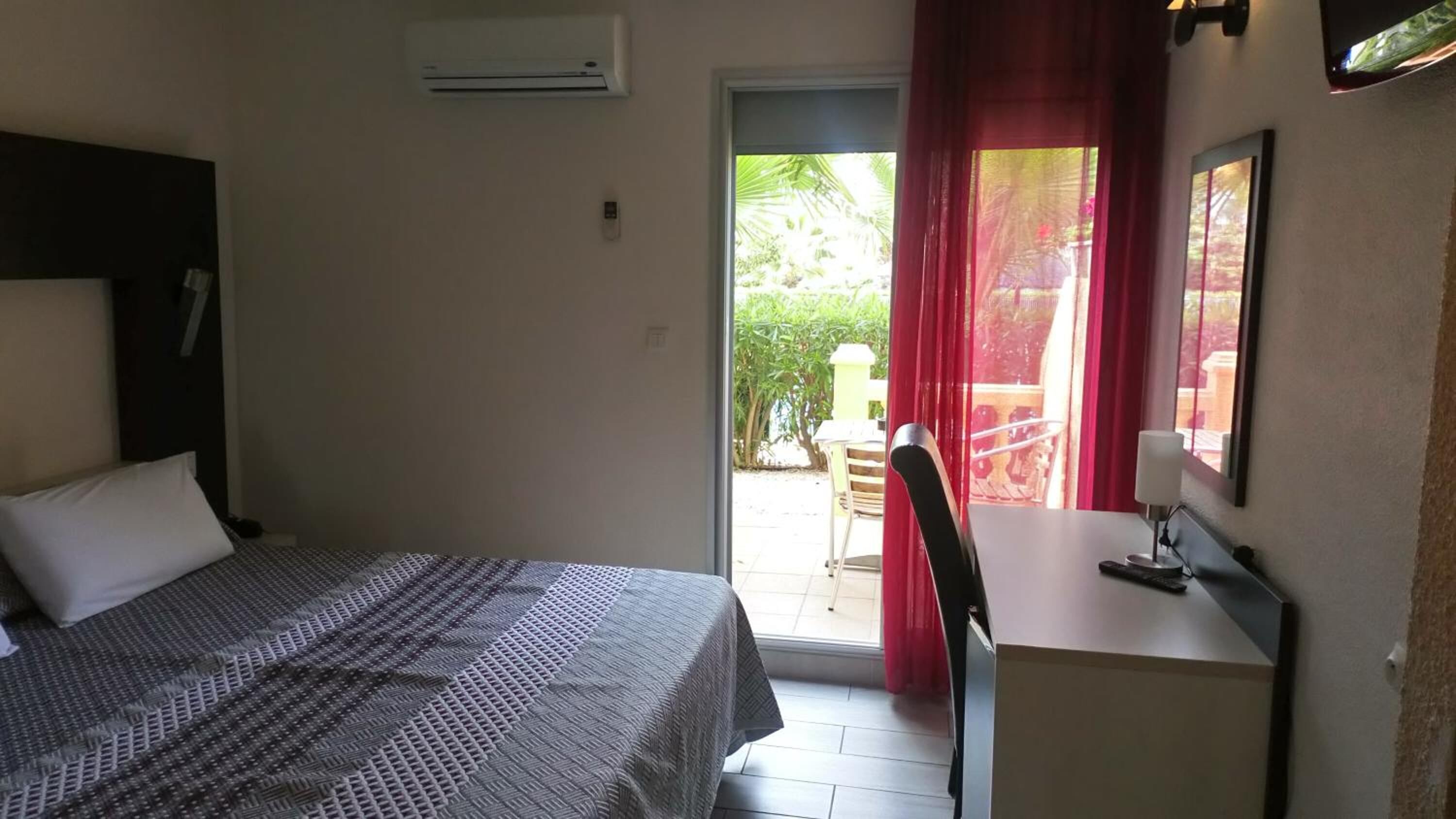Ein Hotelzimmer mit Bett, Schreibtisch, Stuhl und einem Fenster mit roten Vorhängen.