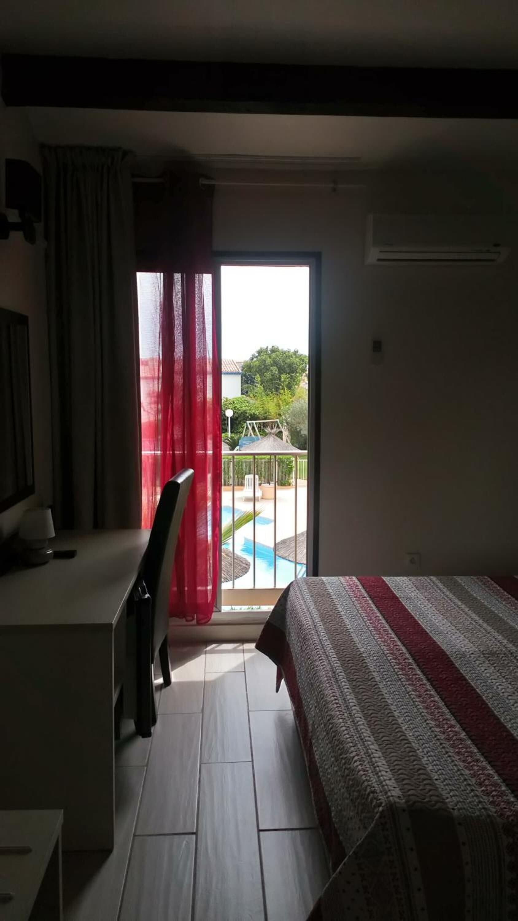 A hotel room with a bed, a desk, and a view of a swimming pool.