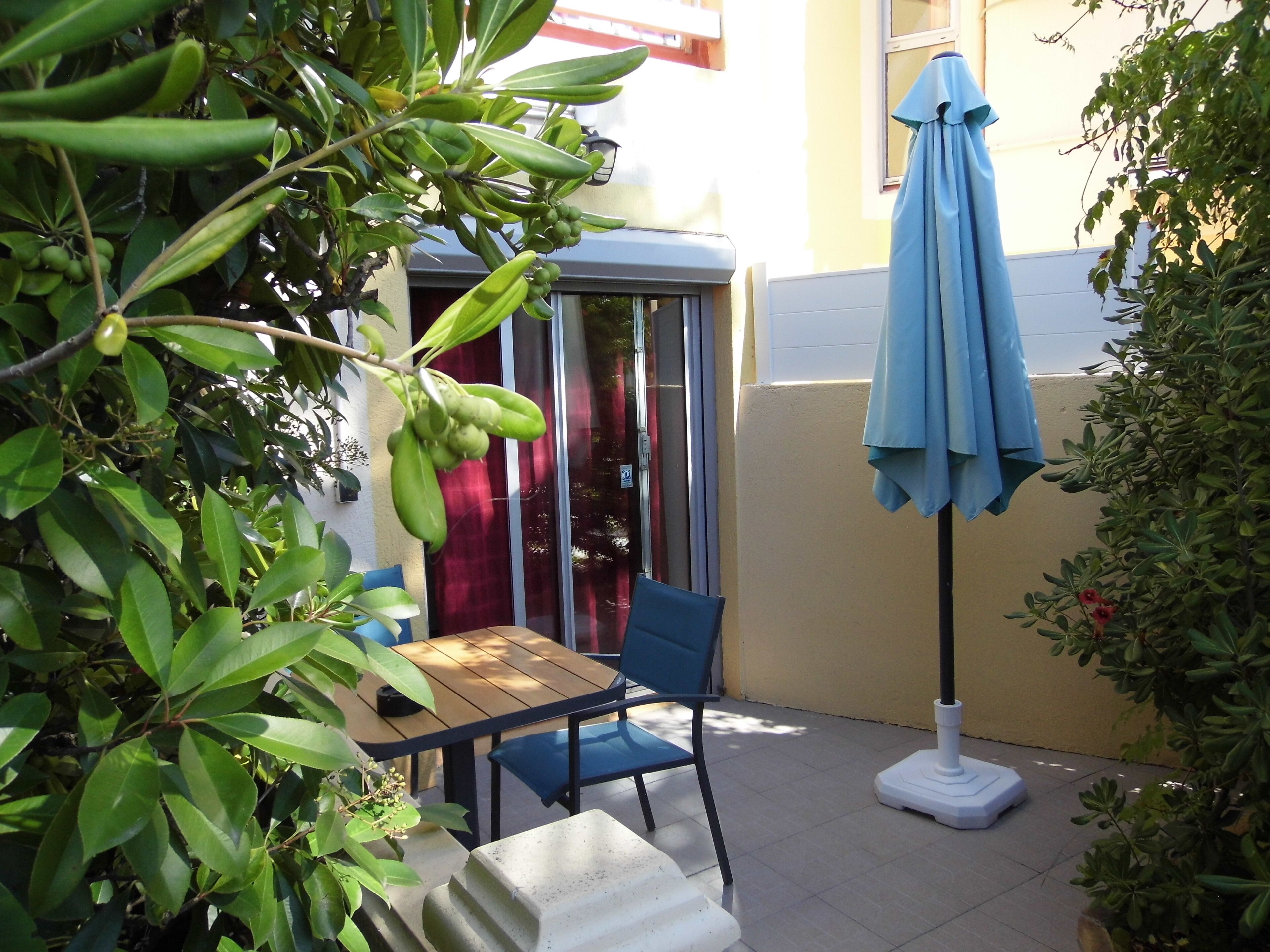 A small outdoor seating area with a table and chairs, a blue umbrella, and a telephone booth.