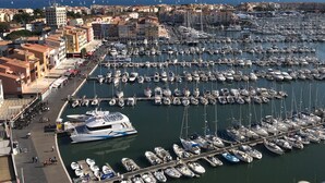 Un puerto deportivo con numerosas embarcaciones amarradas, un yate grande y edificios al fondo.