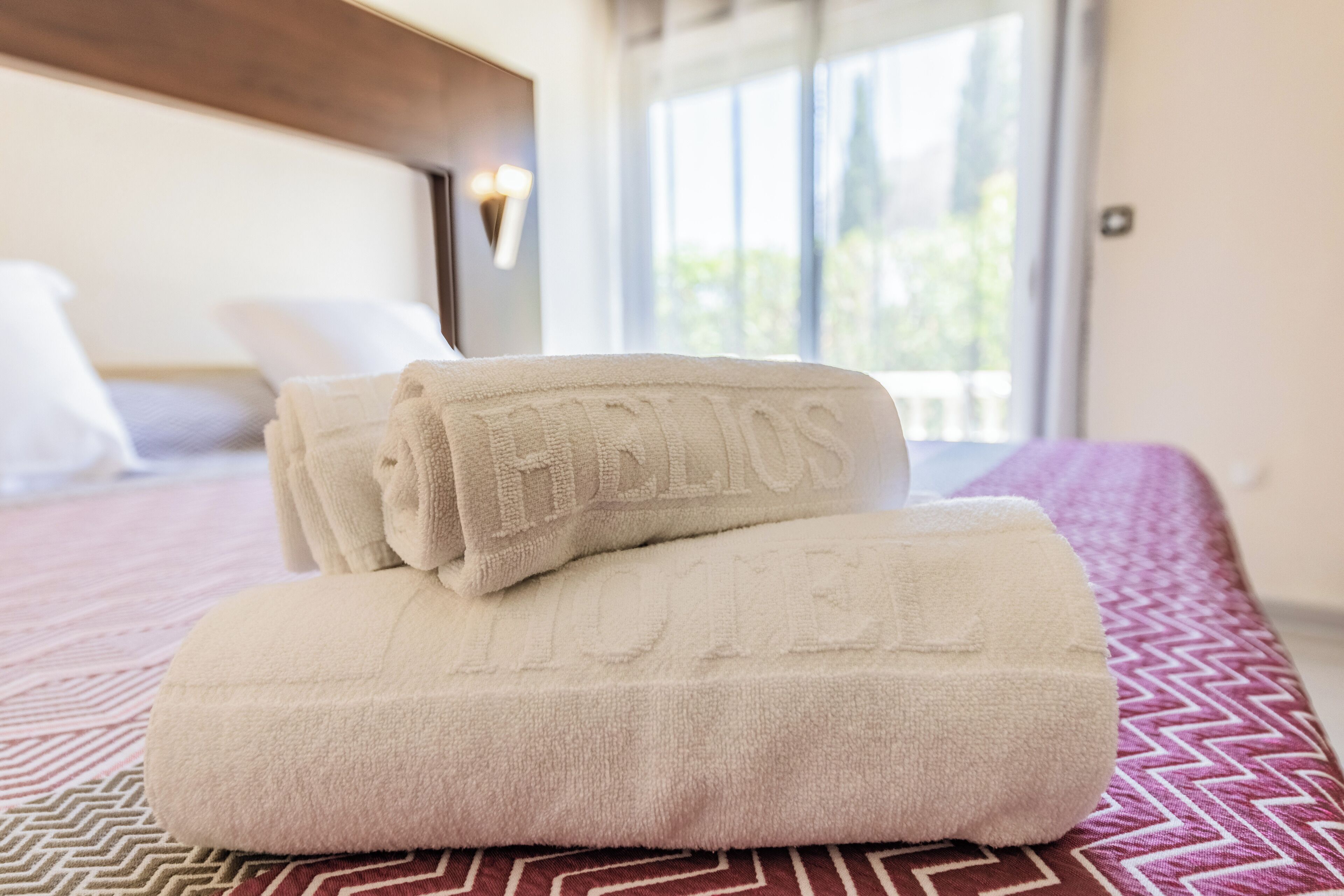 A neatly made bed with folded towels and a patterned bedspread.