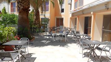 An outdoor patio with tables and chairs, surrounded by buildings and palm trees.