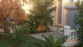 A courtyard with a table and chairs, surrounded by various plants and trees.