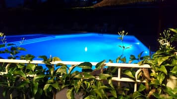 A swimming pool with a clear blue water surface, surrounded by lush green plants and a white railing.