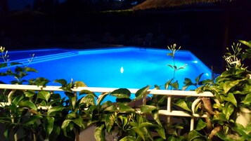Una piscina con superficie de agua azul cristalina, rodeada de exuberante vegetación y una barandilla blanca.