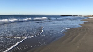Una playa con olas, cielo despejado y montañas a lo lejos.