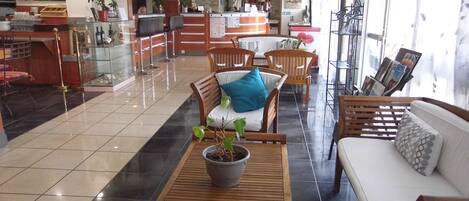 Een hotel lobby met een receptiebalie, zithoek met houten meubels, een potplant en een groot raam met uitzicht.