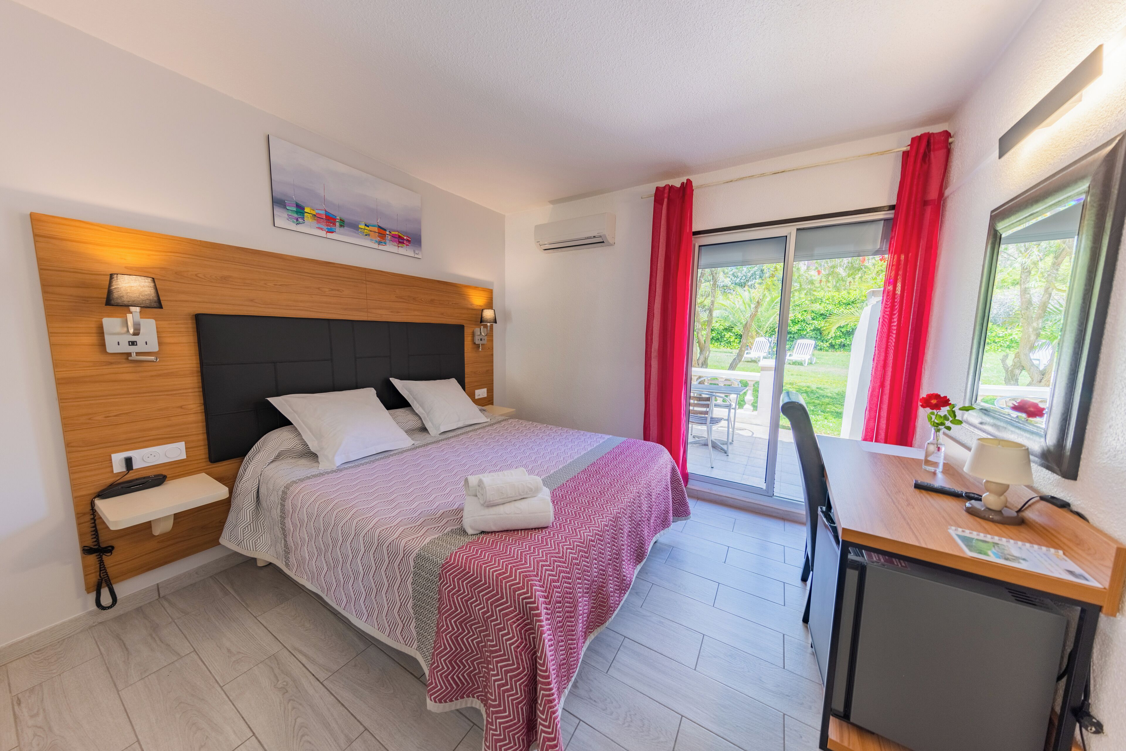 Un dormitorio con cama, mesitas de noche, un escritorio, una silla y una ventana con cortinas.