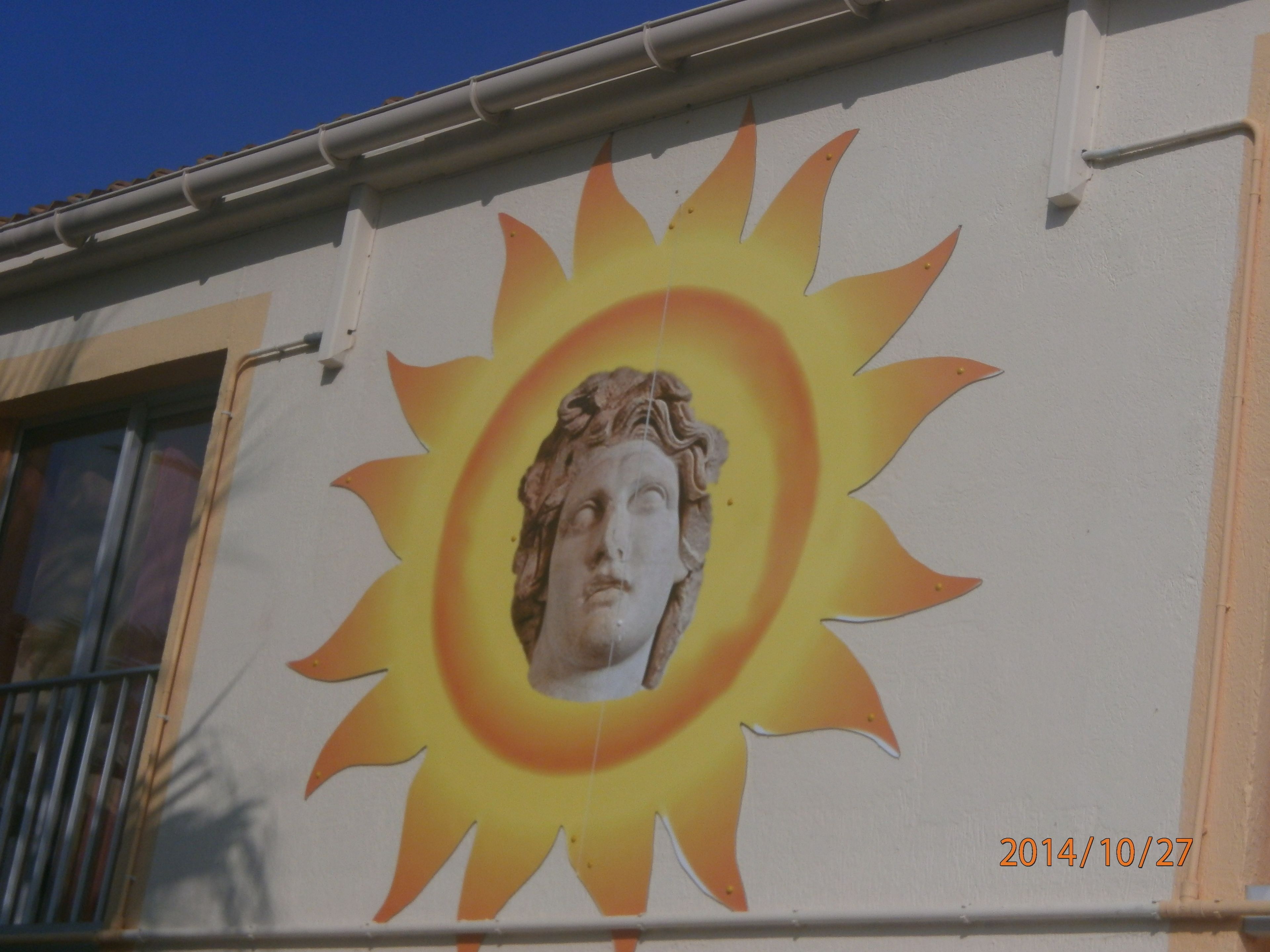 A building with a mural of a sun and a classical statue.