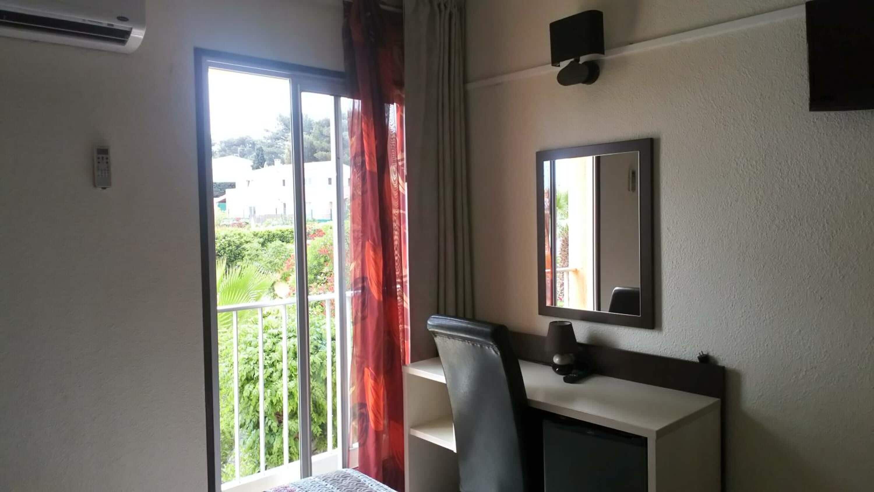 Habitación de hotel con escritorio, silla y ventana grande con cortinas.