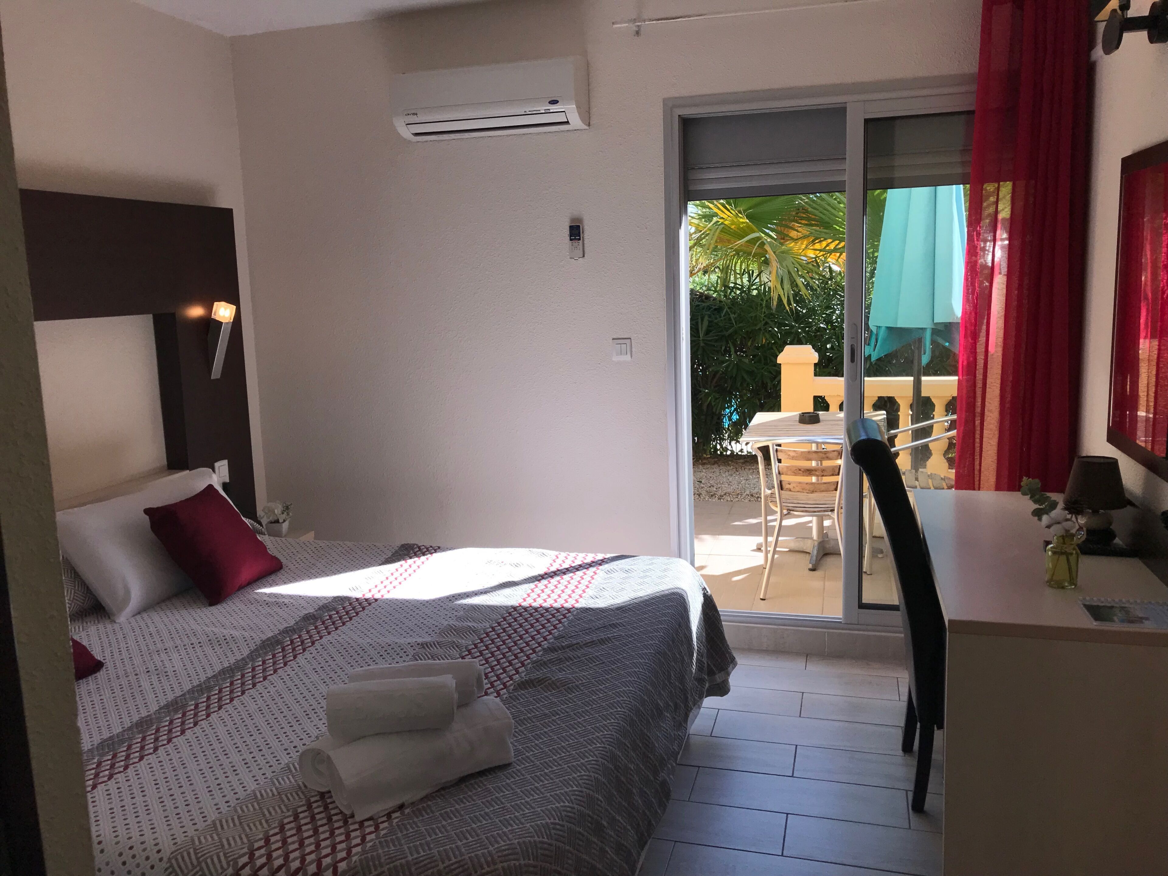 A hotel room with a bed, a small table, a chair, and a balcony with a table and chairs.