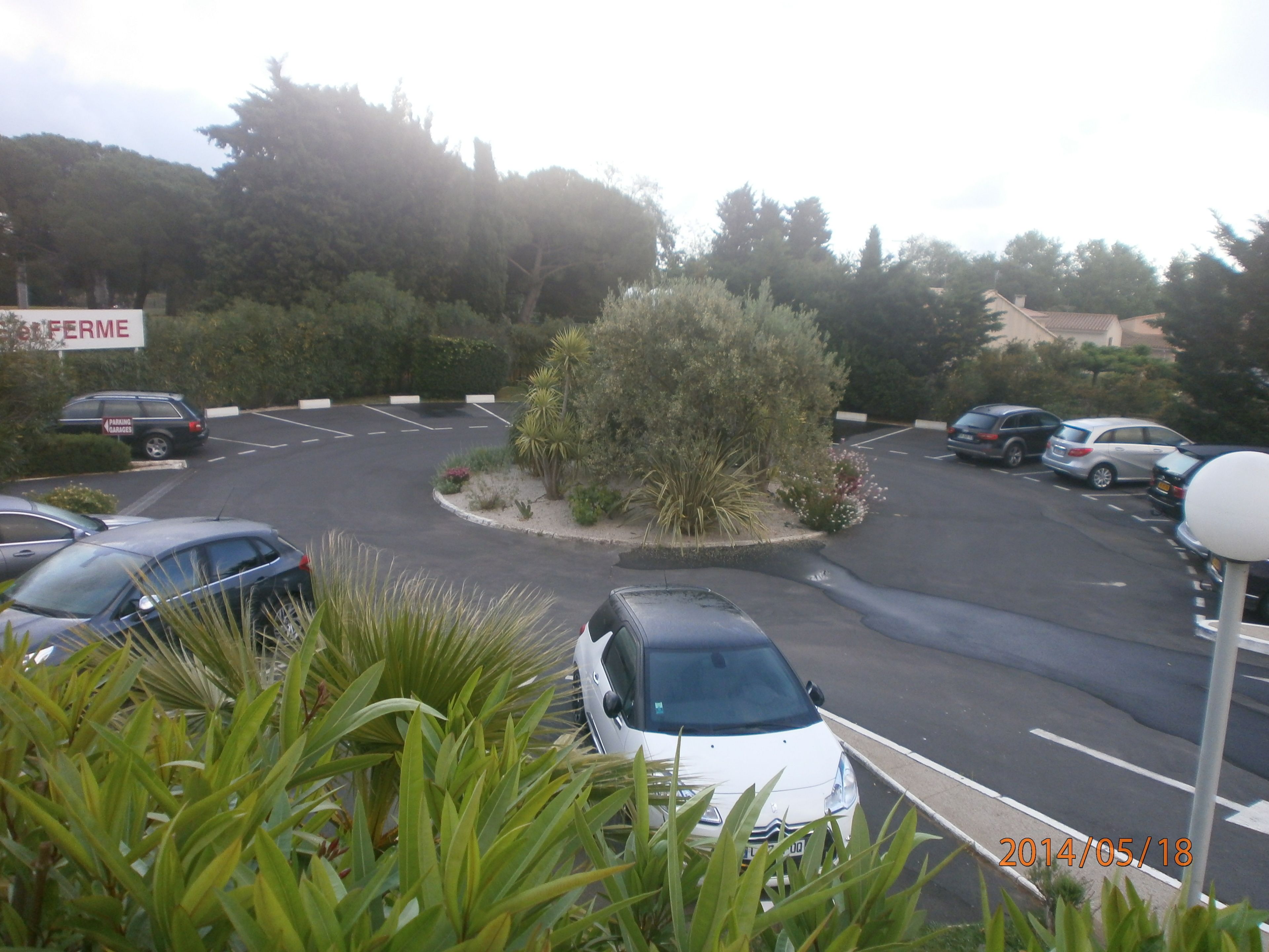 A parking lot with several cars and a central landscaped area with a small tree and shrubs.