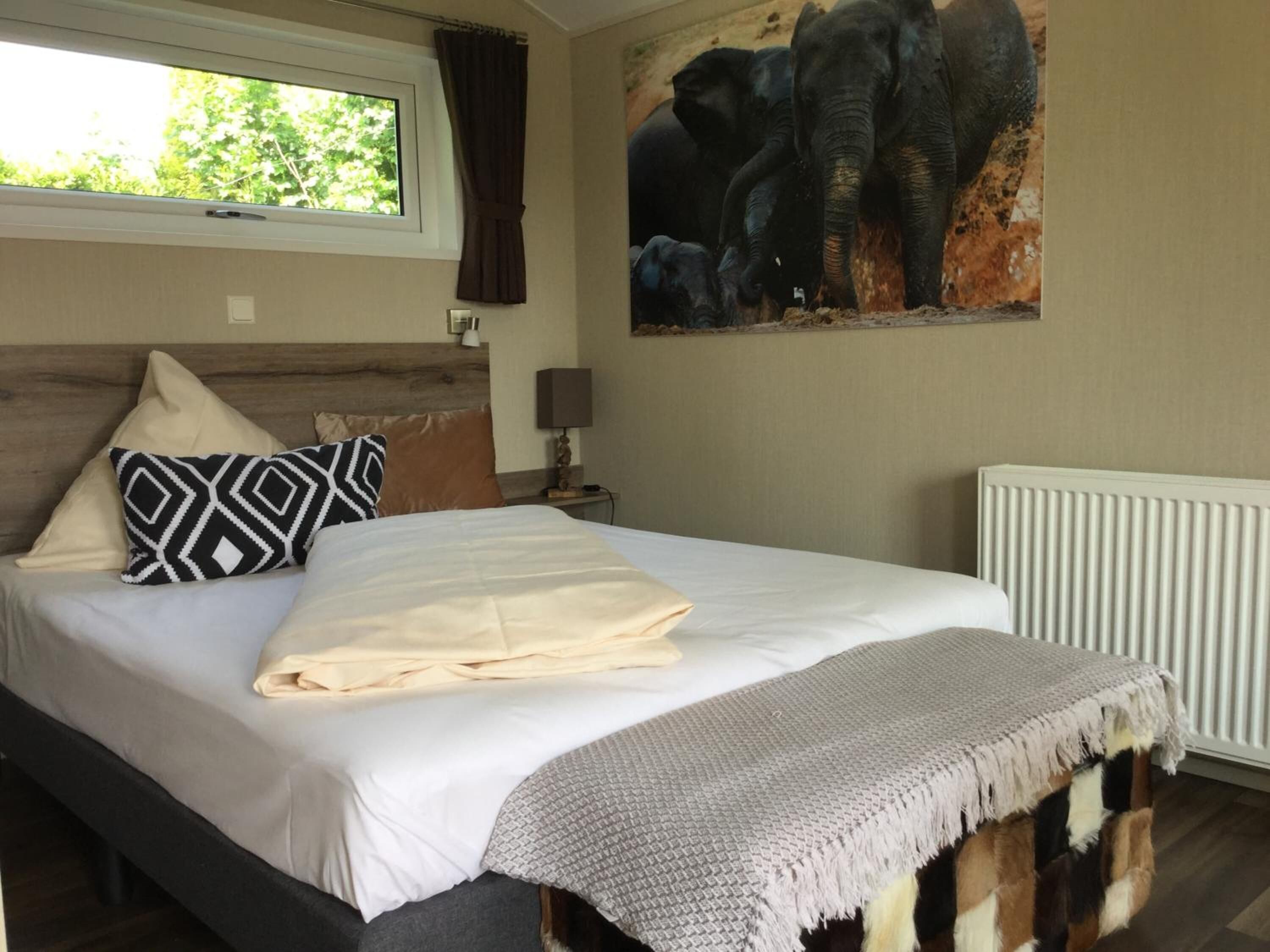 Un dormitorio con una cama grande, cabecera, ventana con cortinas, lámpara de pared y radiador.