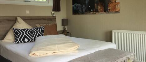 Un dormitorio con una cama grande, cabecera, ventana con cortinas, lámpara de pared y radiador.