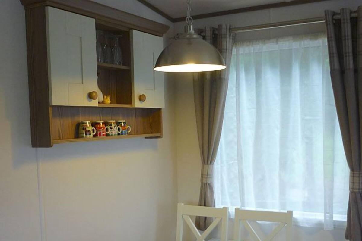 Un coin repas avec une table en bois, des chaises blanches, une lampe suspendue et une étagère contenant des ustensiles de cuisine.