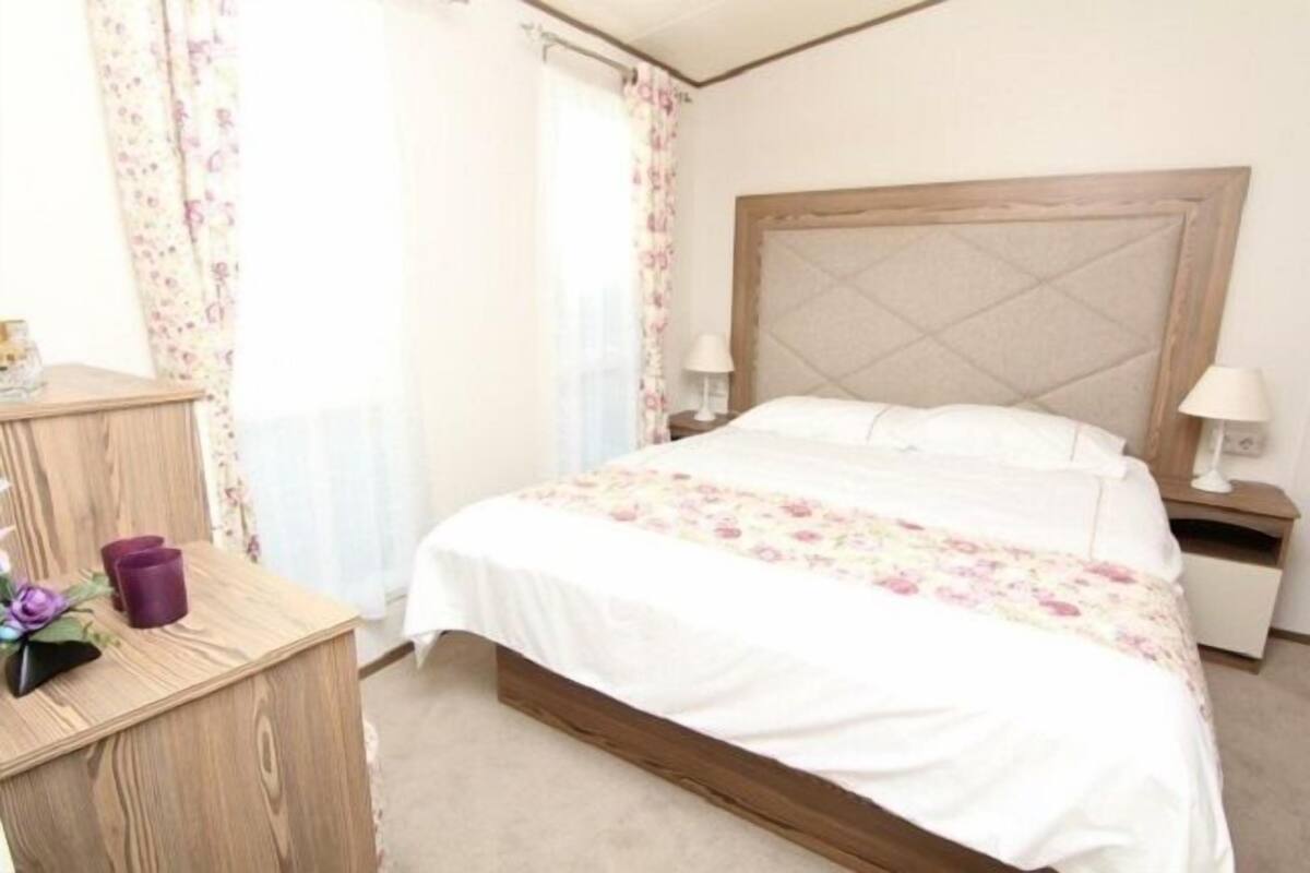 Une chambre à coucher bien rangée, avec un lit en bois, du linge de lit blanc et une table de chevet sur laquelle se trouve une lampe.