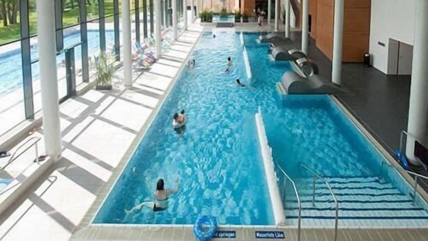 Una piscina interior con agua cristalina, un trampolín y un puesto de socorrista.