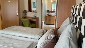 Habitación de hotel con dos camas, un escritorio, una silla y un baño visible a través de una puerta abierta.