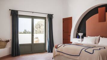 Un dormitorio con cama, ventana con cortinas, mesita de noche con lámpara y un mueble de pared.