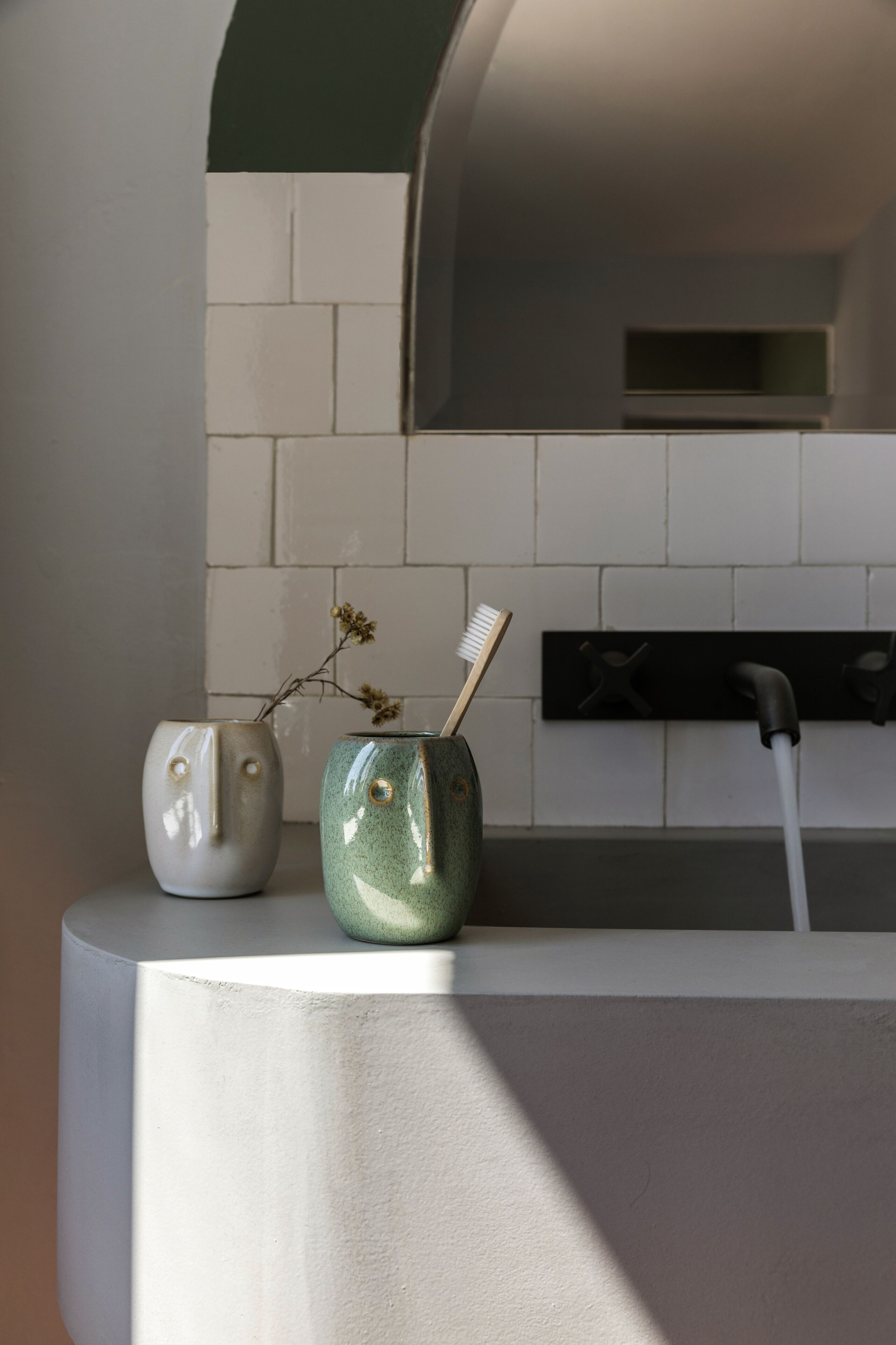 A kitchen with two ceramic vases on a countertop, one with a branch and a toothbrush, and a modern faucet.