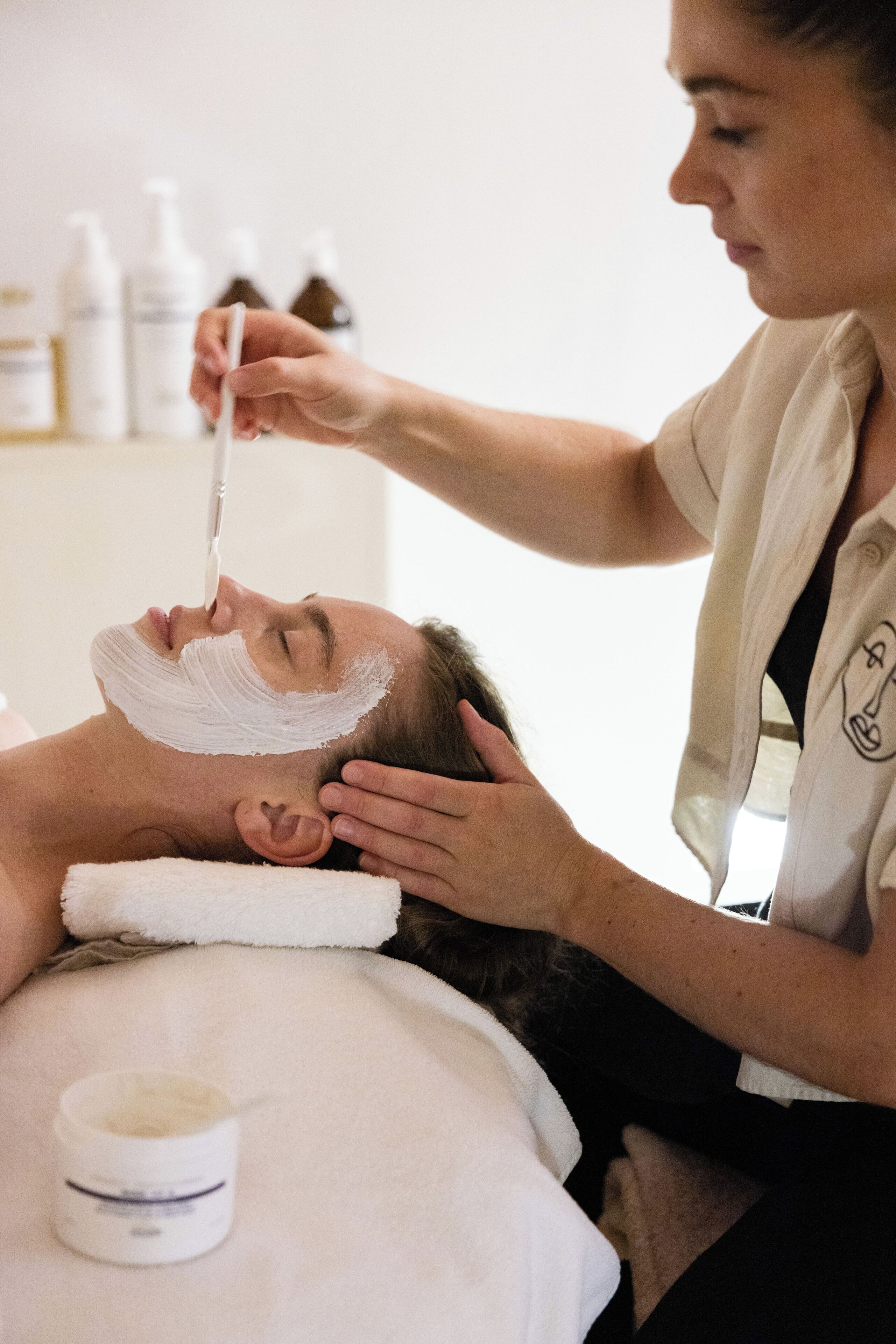 A person lying on a bed with a white towel, receiving a facial treatment.