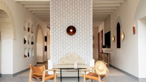 A modern interior with a high ceiling, a central seating area with a table, and a decorative wall with a circular light fixture.
