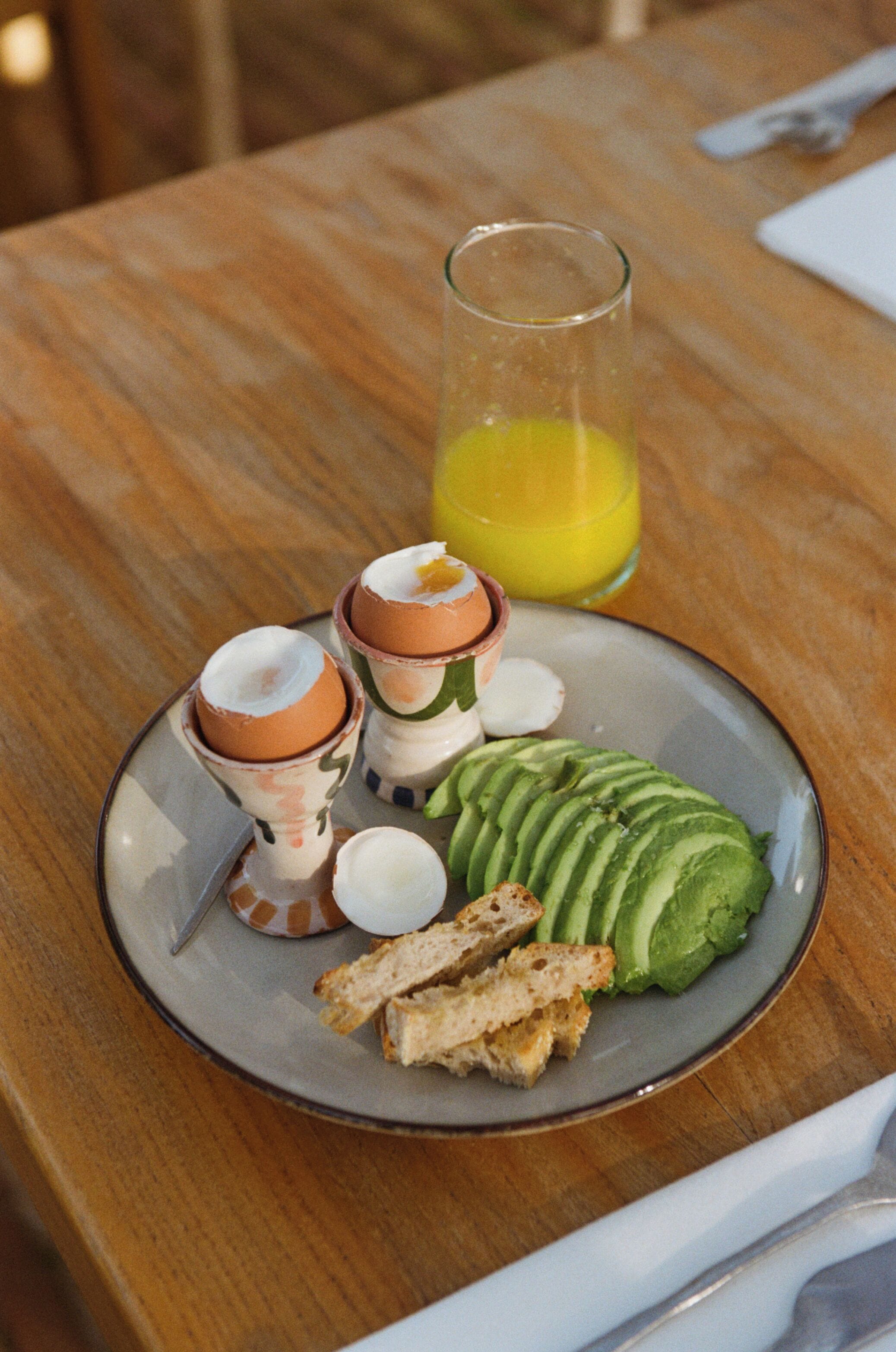 A plate with avocado slices, toast, and two cups of coffee on a wooden table.