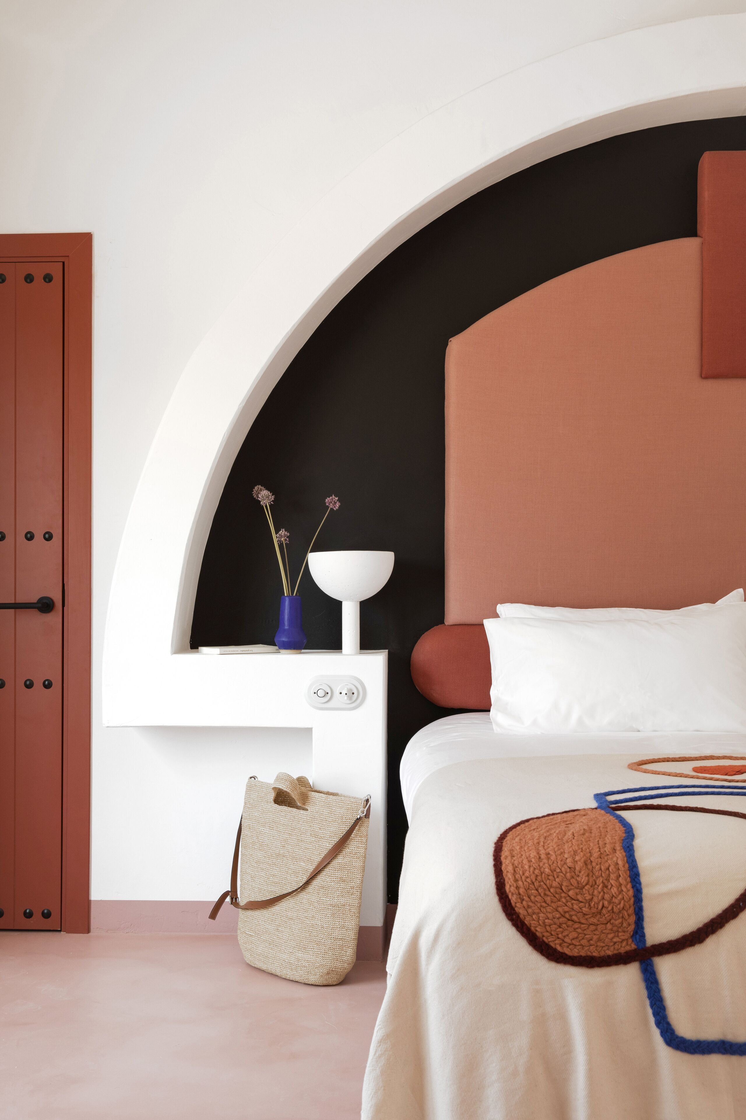 Une chambre à coucher avec un lit, une table de chevet, une étagère fixée au mur et une porte.