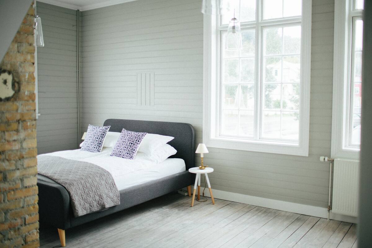 A bedroom with a bed, a small bedside table, a window, and a brick wall.