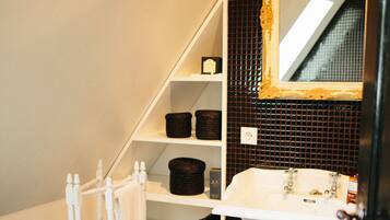 A bathroom with a white pedestal sink, a mirror with a gold frame, a towel rack, and shelves with baskets.