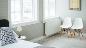A bedroom with a bed, two white chairs, a window, and a radiator. - Hoepfner  Historical House (Akureyri)